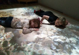 Dziewczynka i chłopiec leżą na wizualizacji oceanu na podłodze interaktywnej